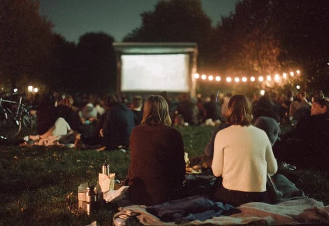 Zwei Menschen schauen nachts Open-Air-Kino auf einer Wiese